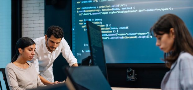 Software developer team working together, discussing on coding on multi computer screen. Software developers checking programming code on computer screen. working through a coding problem together.